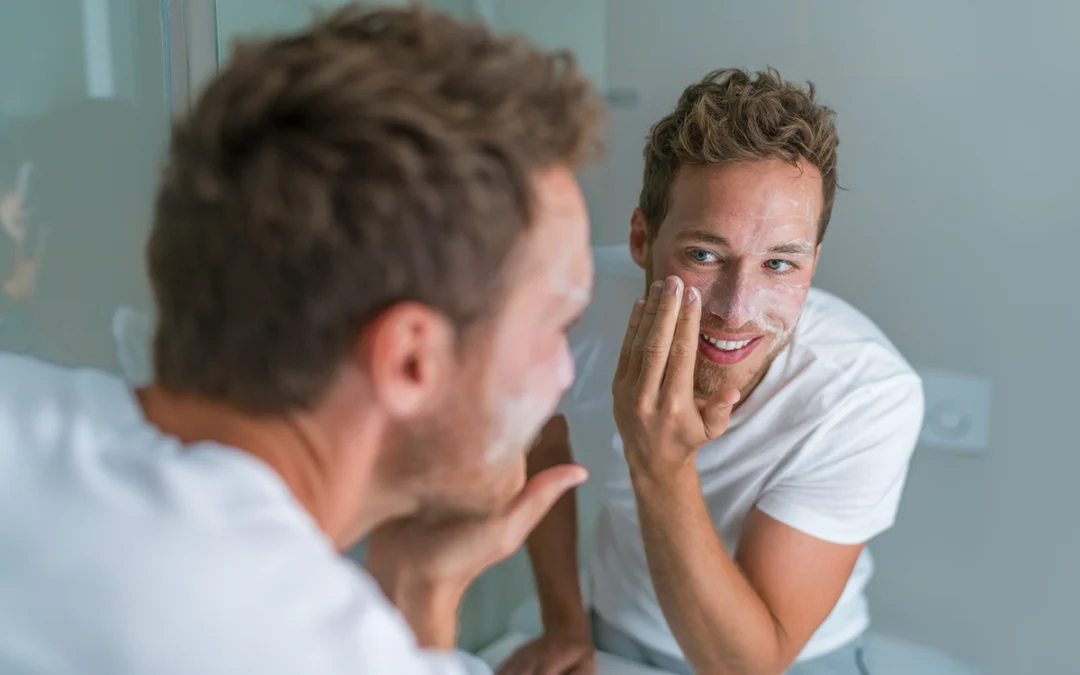Man washing face with soap scrubbing exfoliation mask facial treatment looking in the mirror