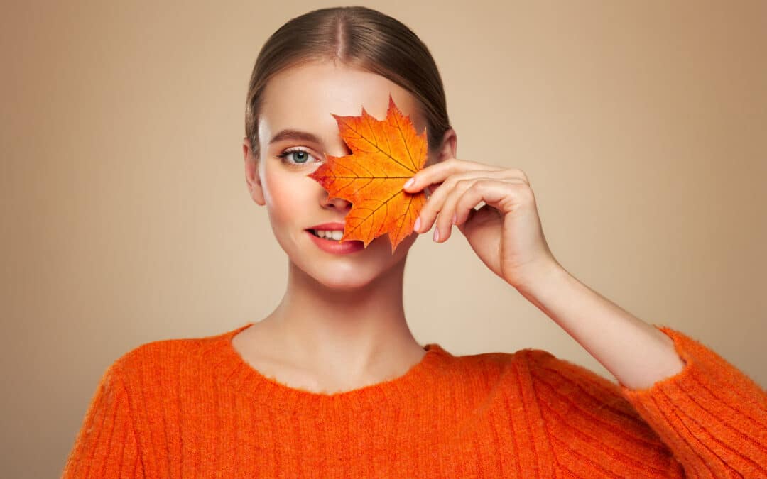 Portrait of beautiful young woman in orange blouse with autumn leafs. Healthy clean fresh skin natural make up beauty eyes